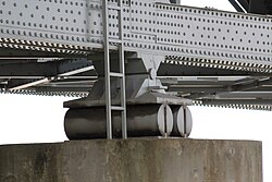 Two cylinders of steel, supporting a large steel bridge, and resting on a concrete support
