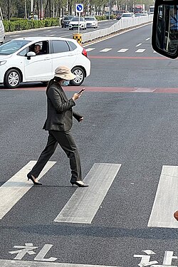 A pedestrian looking down at a smartphone while crossing a road