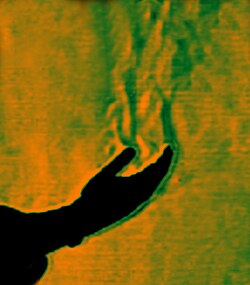 This color schlieren image reveals thermal convection originating from heat conduction from a human hand (in silhouette) to the surrounding still atmosphere, initially by diffusion from the hand to the surrounding air, and subsequently also as advection as the heat causes the air to start to move upwards.