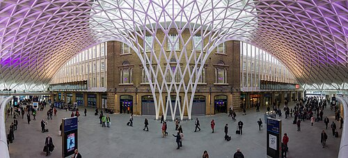 King's Cross following refurbishment in 2012. The steel structure of the roof, engineered by Arup, has been described as being "like some kind of reverse waterfall, a white steel grid that swoops up from the ground and cascades over your head".[65]