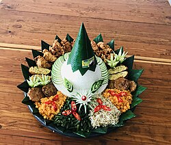 Indonesian festive tumpeng rice cone, garnished with decoratively sliced chili pepper and cucumber.