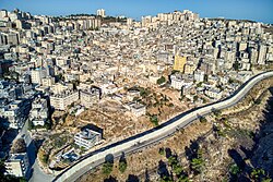 Shu'fat Camp in the city of Jerusalem, 2023. The official area of the camp is in the center of the image and is characterized by low-rise buildings; on either side of the camp are additional Palestinian neighborhoods located beyond the Israeli West Bank barrier (visible at the bottom of the image), where the buildings are taller.