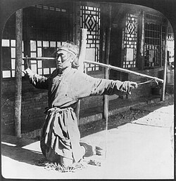 Prisoner kneeling on chains, thumbs supporting arms, photographic print on stereo card, Mukden, China (c. 1906)
