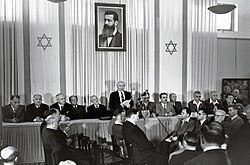 David Ben-Gurion proclaiming Israel's establishment beneath a large portrait of Theodor Herzl