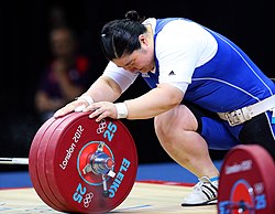An Olympic lifter, Jang Mi-ran, holding a barbell loaded with red 25 kg bumper plates, held in place with a collar. Note the lifter's taped wrists and thumbs, her weightlifting shoes, and her weightlifting belt.