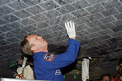 Astronaut Andrew S. W. Thomas takes a close look at TPS tiles underneath Space Shuttle Atlantis.
