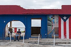 Two men sit by the side of a road with the ocean behind them in Puerto Rico.