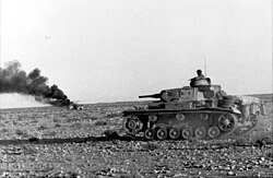 Afrika Korps Panzer III drives past a burning vehicle, April 1941