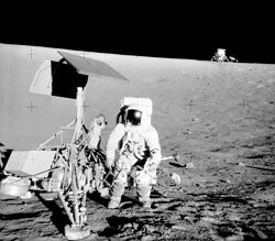 Pete Conrad, commander of Apollo 12, stands next to the Surveyor 3 lander. In the background is the Apollo 12 lander, Lunar Module Intrepid.