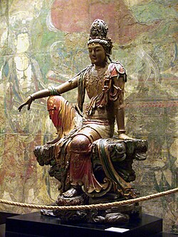 A Liao dynasty polychrome wood-carved statue depicting Guanyin in the Water Moon pose, which raises the right knee and rests the right arm on top of it, symbolizing the divinity of the Pure land, Guanyin's personal paradise, which Guanyin puts off going to until she has saved humanity.