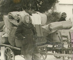 A young Italian exile on the run carries, along with her personal effects, a flag of Italy, during the Istrian-Dalmatian exodus.