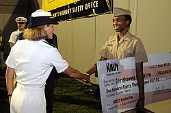 A Navy Rear Admiral presents a Midshipman with a ceremonial cheque symbolizing her $180,000 Navy Reserve Officers Training Candidate scholarship.