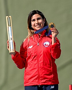 Chilean skeet shooter Francisca Crovetto holding the gold medal she won in the women's skeet in Paris in 2024, as well as a box with an official poster given to all medalists.