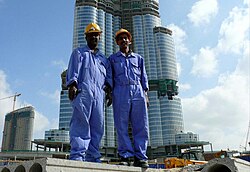 Two South Asian blue-collar workers posing for a picture with the Burj Khalifa on the background
