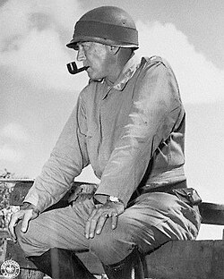 Major General George S. Patton sitting on a fence and smoking a pipe while observing 1941 maneuvers in Louisiana