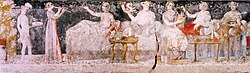 A banquet scene from a Macedonian tomb of Agios Athanasios, Thessaloniki, 4th century BC; shown are six men reclining on couches, with food arranged on nearby tables, a male servant in attendance, and female musicians providing entertainment.[311]