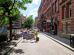 A canal as photographed from a bridge over it. On the left-hand side there is a brick industrial building that is in shadow; on the right-hand side there are brick buildings with many windows facing over the canal, which is lined by brick wall.