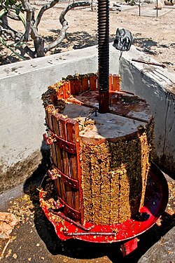 A basket press with half of its slats removed to show the compact pomace "cake" that develops from the leftover skins, seeds and stems after pressing. This cake needs to be cleaned out and removed after each batch.