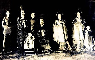 The royal family members in 1915, from left: Yi Kang, Prince Imperial Ui; Yi Cheok, Emperor Sunjong; Yi Un, Prince Imperial Yeong; Gojong; Empress Yun; Lady Kim, Consort Princess Imperial Ui; and Yi Geon. The child in the front row is Princess Deokhye. This is a compilation of individual photographs, since the Japanese did not allow them to be in the same room at the same time, and some were forced to leave Korea.