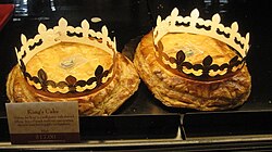 King cakes of the type locally called "French style" on display at the chain bakery/restaurant "La Madeline" branch in Carrollton, New Orleans. They come with cardboard "crowns" to be worn by whoever gets the slice with the token and becomes monarch of the event.