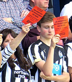 Newcastle fans show "Mike Ashley Out" cards away to QPR, May 2015.