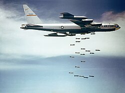 Against a blue sky with white clouds, a B-52F releases bombs over Vietnam
