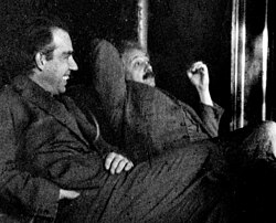 Two men sitting, looking relaxed. A dark-haired Bohr is talking while Einstein looks skeptical.