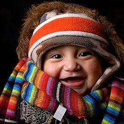 A baby wearing many items of soft winter clothing: headband, cap, fur-lined coat, scarf, and sweater