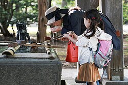 A mother and daughter purify themselves before entering a Shinto shrine.