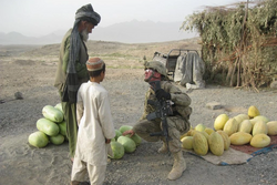 A soldier purchases fresh melons from a local merchant in Shah Wali Kot district, Afghanistan