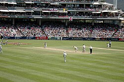 A Test match between South Africa and England in January 2005. The men wearing black trousers are the umpires. Teams in Test cricket, first-class cricket and club cricket wear traditional white uniforms and use red cricket balls.