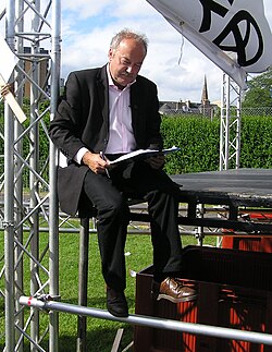 Galloway signing an asylum seekers petition, sitting on the edge of the StWC stage at the 2005 Make Poverty History rally.