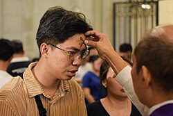 A lay minister draws a cross of ashes on a worshipper's forehead, the prevailing form in English-speaking countries.[69]