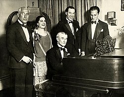 A birthday party honoring French pianist Maurice Ravel in 1928. From left to right: conductor Oskar Fried, singer Éva Gauthier, Ravel (at piano), composer-conductor Manoah Leide-Tedesco, and composer George Gershwin.