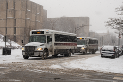 Two University of Chicago shuttle buses (with "UGo" red branding on the sides) on 57th Street outside the Regenstein Library during a snowstorm