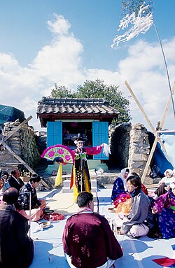 Brightly clothed people, one holding a paper fan, performing a ritual at daytime