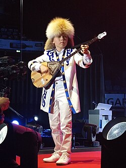 A Kazakh boy playing dombra in traditional clothing during an IFLC Festival