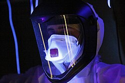 A person wearing full protective gear, glowing in ultraviolet light