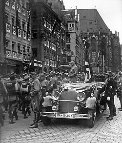 Hitler saluting troops from atop his staff car, a Mercedes-Benz 770k.
