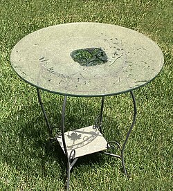 In season, pollen can cover objects with a thick layer. The center of this glass-top table had been covered before the photo was taken, allowing the grass beneath the table to now be visible while the surrounding pollen layer is opaque.