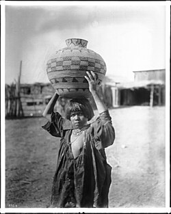 Apache Indian girl carrying an olla (a water basket) on her head, c. 1900