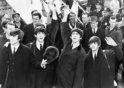 Pop music group The Beatles arriving at an airport and waving to fans