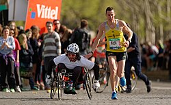 A runner gives a friendly tap on the shoulder to a wheelchair racer during the Marathon International de Paris (Paris Marathon) in 2014.