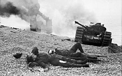 Canadian wounded and abandoned Churchill tanks after the raid. A landing craft is on fire in the background.