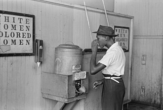 African-American man drinking from a "Colored" water cooler in streetcar terminal, Oklahoma City, July 1939