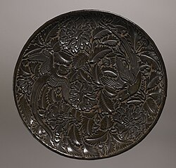 A plate made of lacquer, wood, and paper from the Yuan dynasty. The Chinese were able to perfect a method of making lacquer. Decorating this plate are parrots and peonies. The parrot was a symbol of fidelity; because of its ability to mimic human speech, it was believed to be a suitable companion to a woman whose husband was away from home. The bird would be able to inform each person of the other's activities. The peony was a symbol of female virtue. When shown in full bloom, it is a token of love, affection, and feminine beauty.[113] Birmingham Museum of Art.