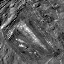 The Inverness Corona is characterized by its white central "chevron". The crater Alonso is visible in the upper right, as well as the cliffs of Argier Rupes in the upper left.