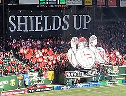 A tifo combining held shields and multiple hoisted painted banners at Providence Park in Portland, Oregon, U.S.