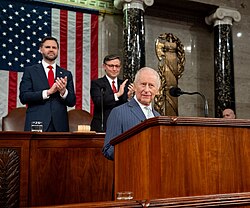 King Charles at a lectern with Vance and Mike Johnson behind him. His wife, Queen Camilla, is next to him