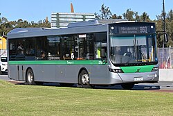 Light green, orange, and white bus stopping in front of multi-story building.